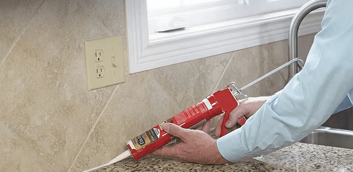 Handyman applying caulk along a kitchen backsplash and countertop seam in Irvine, CA