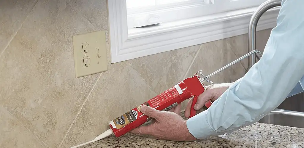 Handyman applying caulk along a kitchen backsplash and countertop seam in Irvine, CA